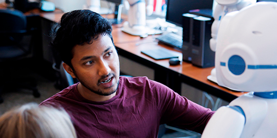 Image of a male student looking at a robot in the AI Robotics lab