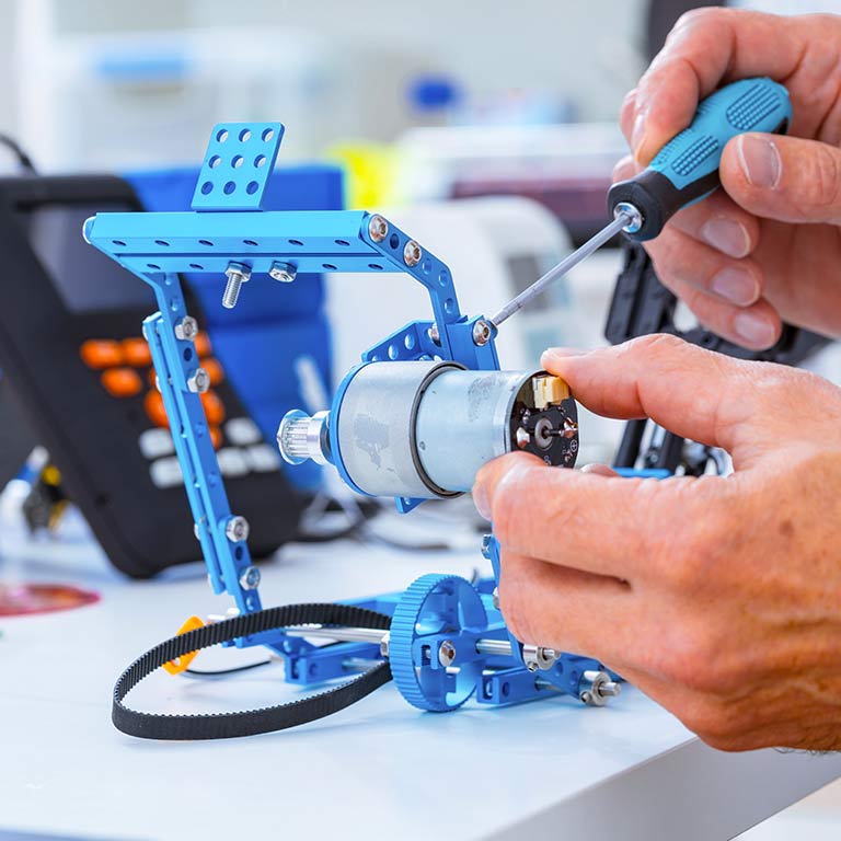 Close-up of hands as they work on a blue metal electronic device in a makerspace lab in Luddy Hall