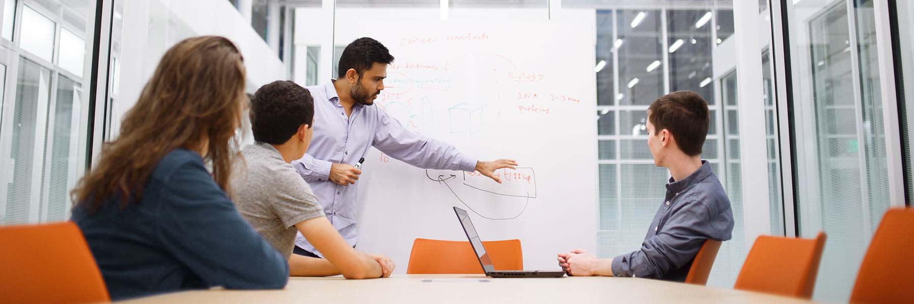 A faculty member writes on a whiteboard as he speaks to students in a room in Luddy Hall.