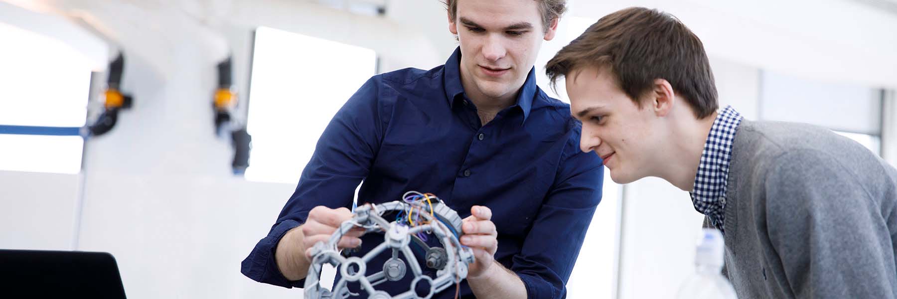 Two students examine a electronic device shaped to fit on the head as part of their project.