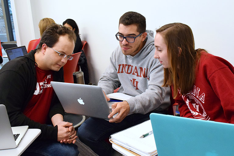 A group of three students share a laptop during in-class work.