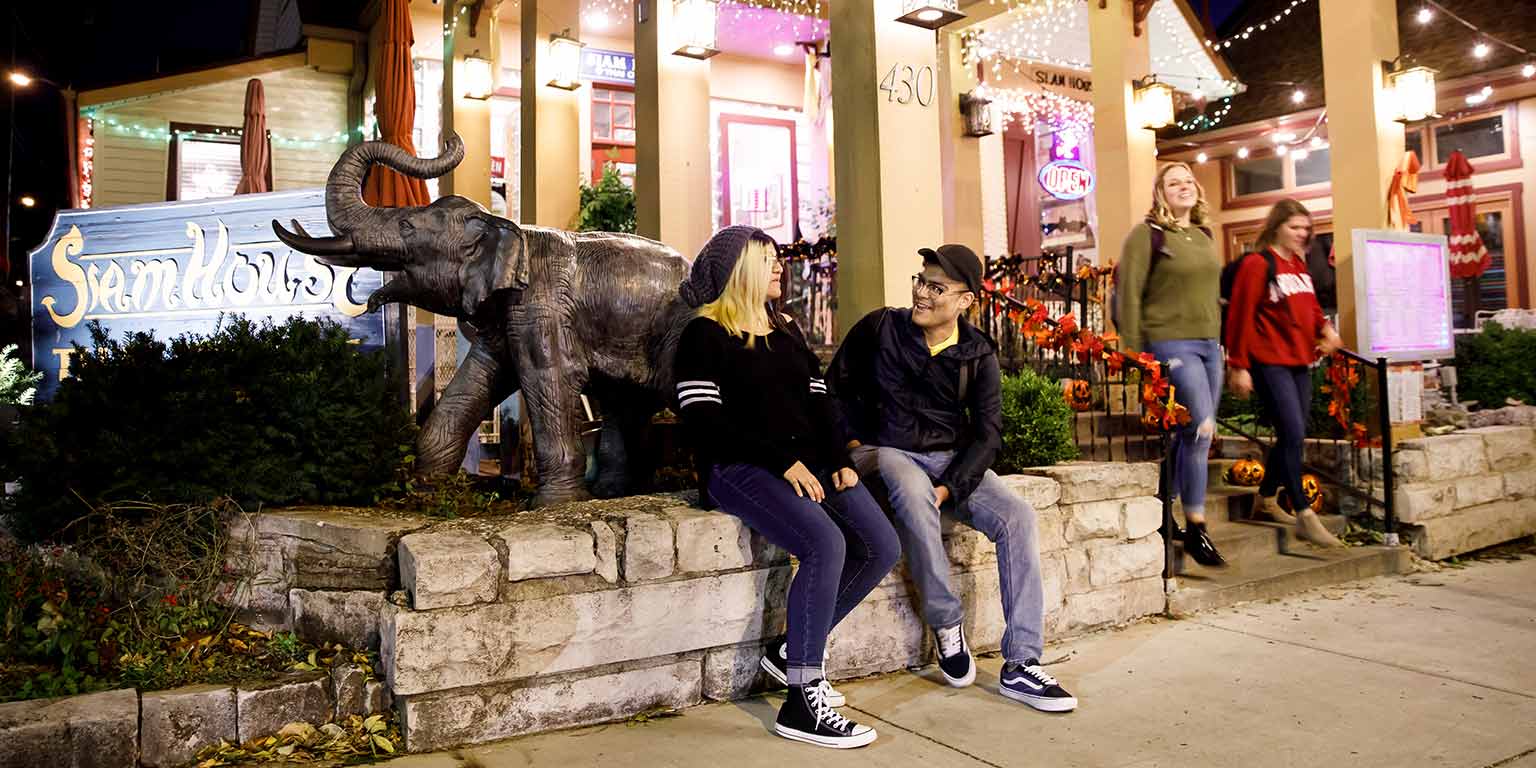 Two students sit outside Siam House restaurant and chat as two other students leave the restaurant.