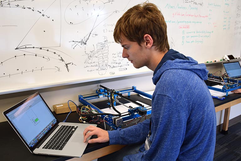 A SICE summer camp participant works with his laptop and a piece of automated drawing technology.